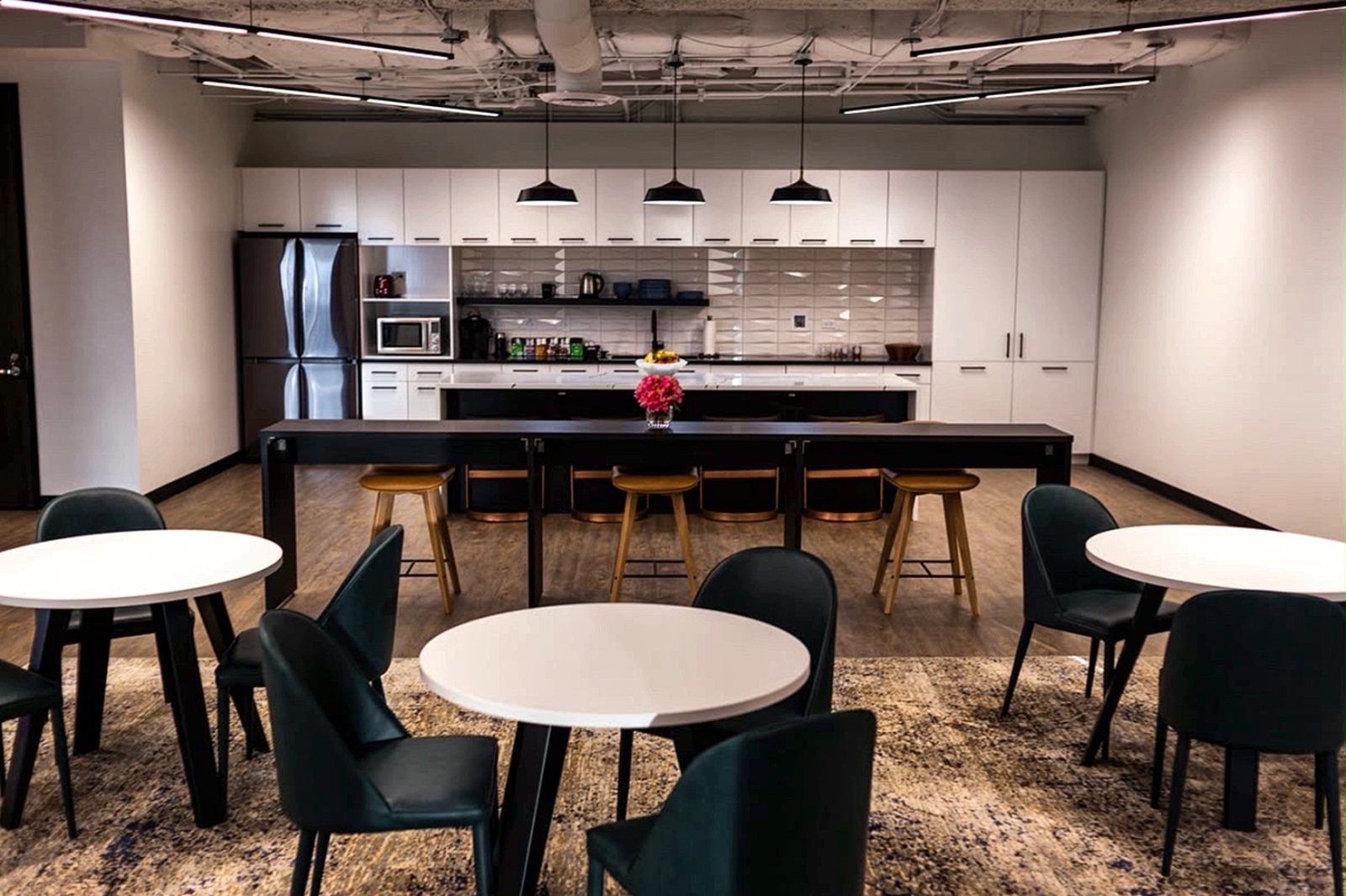 Open office cafe with white cabinetry, pendant lights and green upholstered chairs